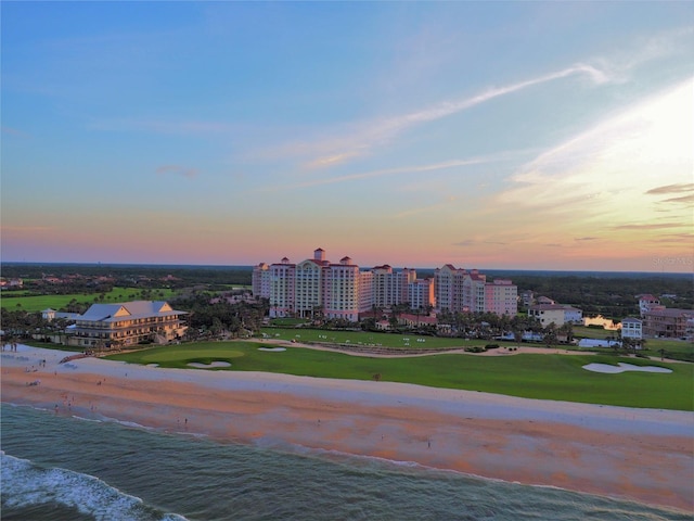 aerial view at dusk featuring a water view and a view of the beach