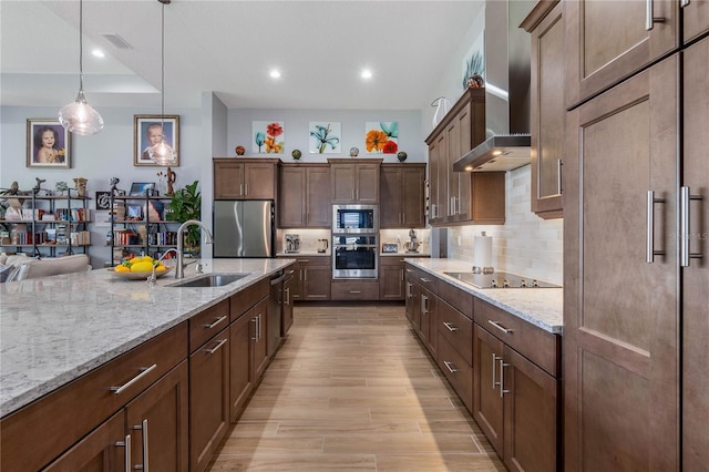 kitchen with sink, decorative light fixtures, stainless steel appliances, light stone countertops, and wall chimney range hood