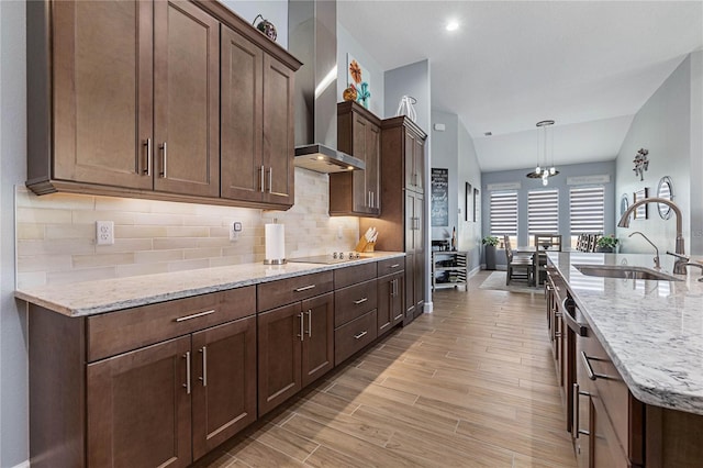 kitchen with decorative light fixtures, sink, light stone counters, wall chimney range hood, and black electric cooktop