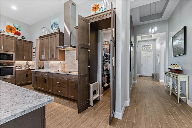 kitchen with built in microwave, backsplash, hanging light fixtures, stainless steel oven, and wall chimney exhaust hood