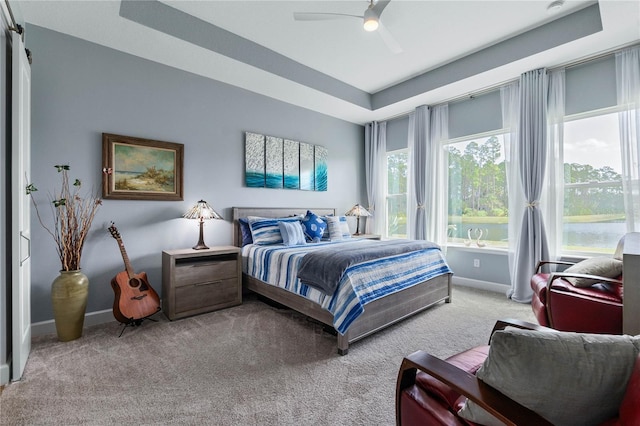 bedroom featuring a raised ceiling, light carpet, and ceiling fan