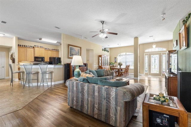 living room featuring a ceiling fan, a textured ceiling, visible vents, and dark wood-type flooring