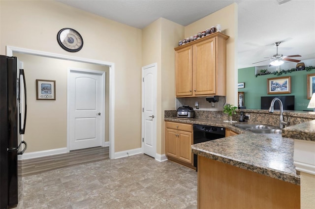 kitchen featuring dark countertops, a sink, black appliances, a peninsula, and baseboards