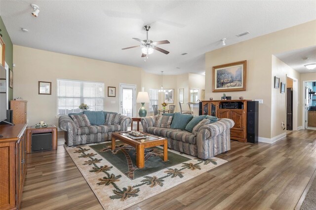 living room with dark wood-type flooring, visible vents, ceiling fan, and baseboards