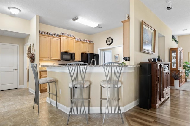 kitchen featuring light brown cabinets, a peninsula, a kitchen breakfast bar, light countertops, and black appliances