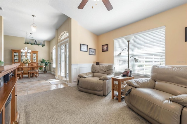 living room featuring light carpet, wainscoting, light tile patterned flooring, a decorative wall, and ceiling fan with notable chandelier