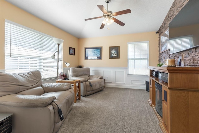 living room with a ceiling fan, light colored carpet, lofted ceiling, a wainscoted wall, and a decorative wall