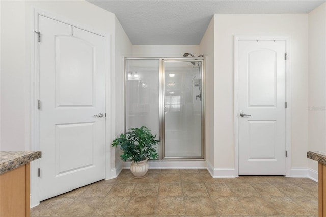 full bathroom featuring a stall shower, baseboards, a textured ceiling, and vanity