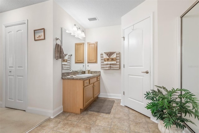 bathroom with a closet, visible vents, vanity, a textured ceiling, and baseboards