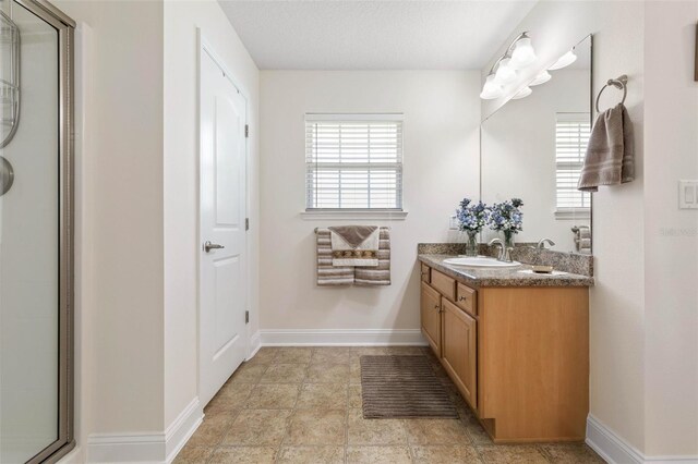 full bath featuring a textured ceiling, an enclosed shower, vanity, and baseboards