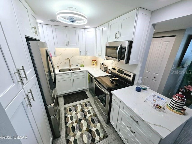 kitchen with sink, stainless steel appliances, tasteful backsplash, light stone countertops, and white cabinets