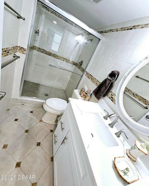 bathroom featuring tile patterned flooring, vanity, an enclosed shower, and toilet