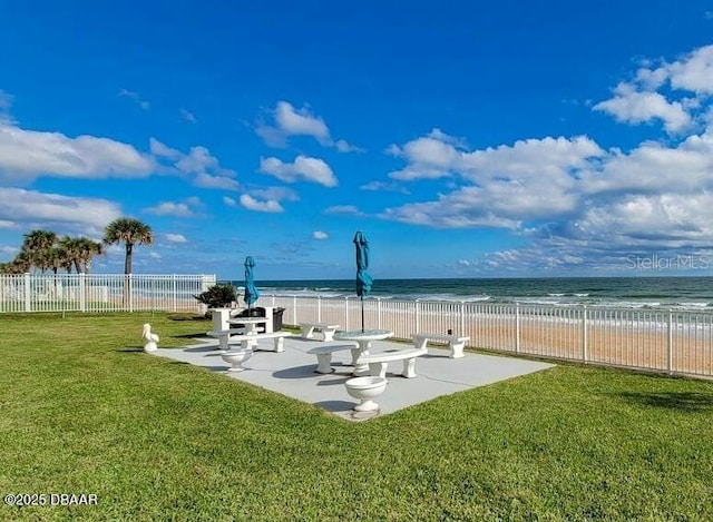 view of property's community with a water view, a view of the beach, a patio, and a lawn