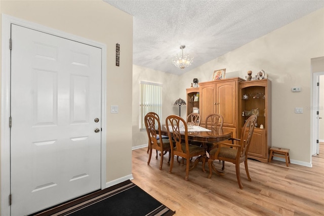 dining space featuring an inviting chandelier, vaulted ceiling, a textured ceiling, and light hardwood / wood-style flooring