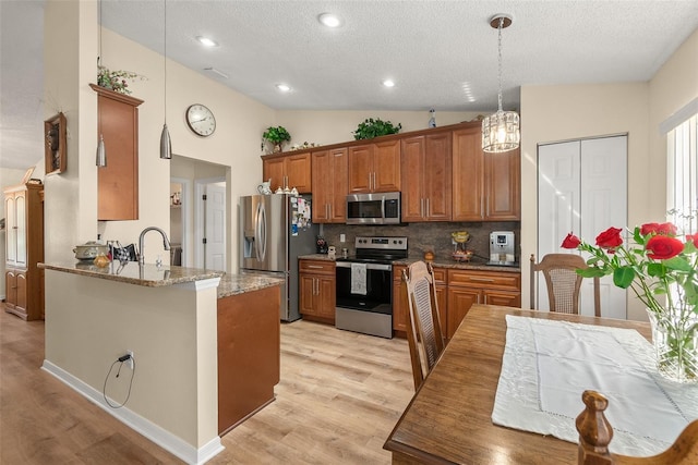 kitchen featuring kitchen peninsula, lofted ceiling, stainless steel appliances, decorative light fixtures, and dark stone counters