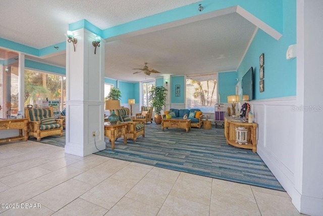 tiled living room with ceiling fan, a textured ceiling, and ornate columns