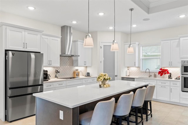 kitchen with white cabinets, a center island, stainless steel appliances, wall chimney range hood, and a sink