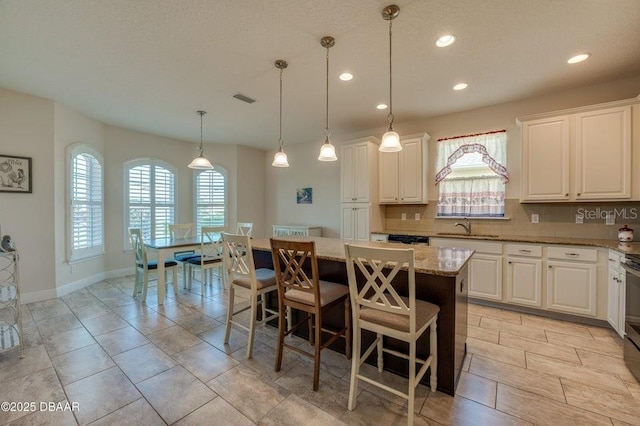 kitchen featuring white cabinetry, light stone counters, a center island, a kitchen breakfast bar, and pendant lighting