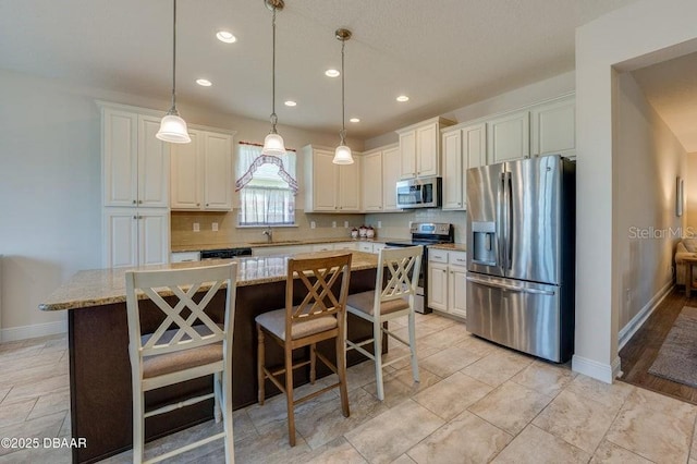 kitchen with a breakfast bar, appliances with stainless steel finishes, a center island, light stone countertops, and decorative light fixtures