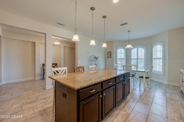 kitchen with hanging light fixtures, a center island, dark brown cabinetry, and light stone counters