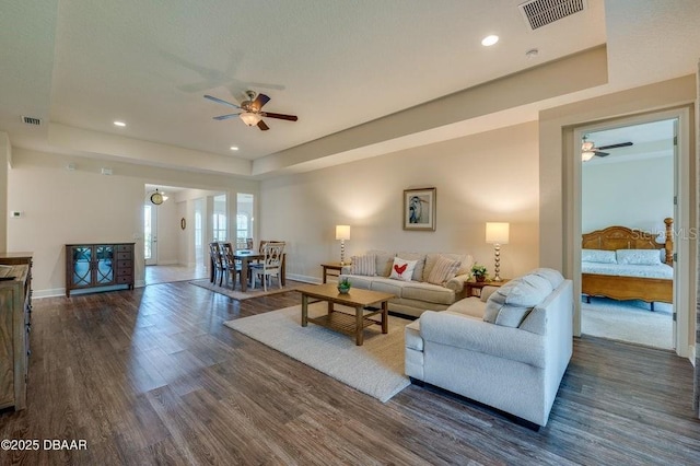 living room featuring ceiling fan, a tray ceiling, and dark hardwood / wood-style flooring