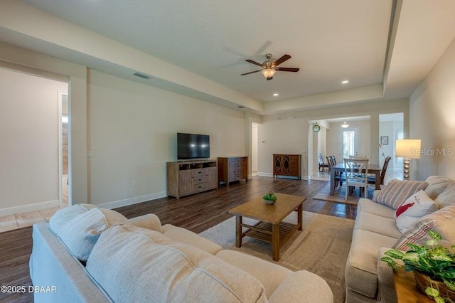 living room featuring hardwood / wood-style flooring, ceiling fan, and a raised ceiling