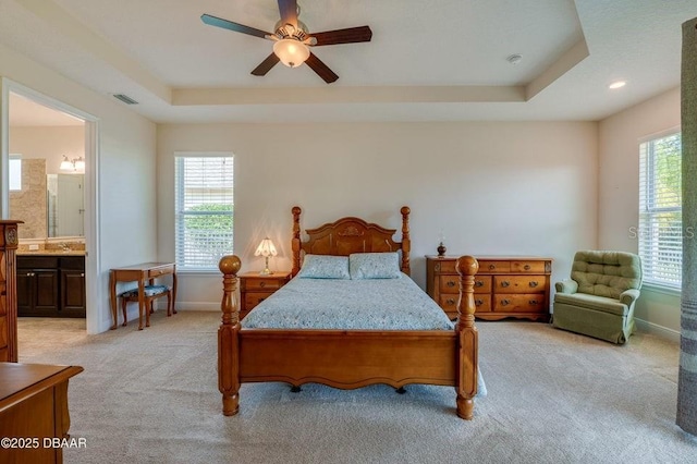 bedroom with multiple windows, connected bathroom, light colored carpet, and a raised ceiling