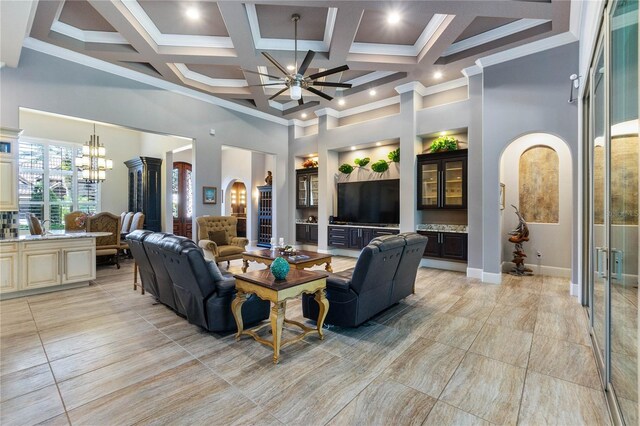 living room with coffered ceiling, crown molding, built in features, a towering ceiling, and ceiling fan with notable chandelier