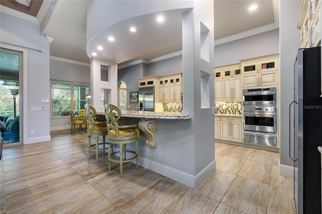 kitchen featuring a breakfast bar, stainless steel appliances, light stone countertops, decorative backsplash, and cream cabinetry