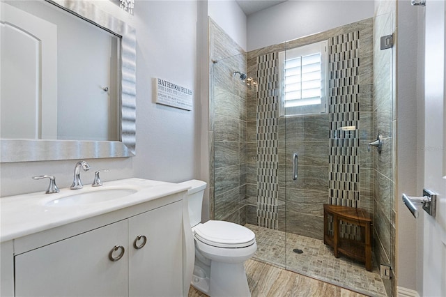 bathroom featuring vanity, wood-type flooring, a shower with shower door, and toilet