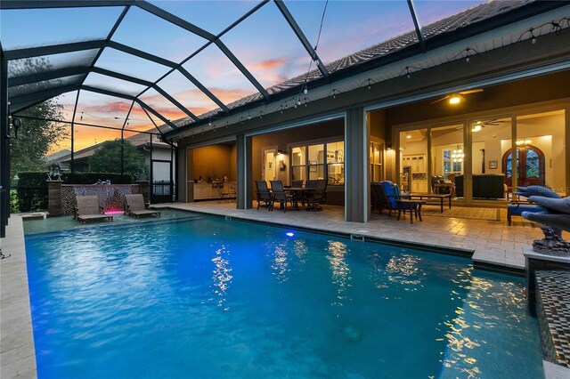 pool at dusk featuring outdoor lounge area, glass enclosure, and a patio area