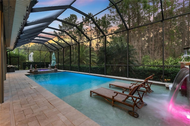 pool at dusk with an in ground hot tub, glass enclosure, and a patio