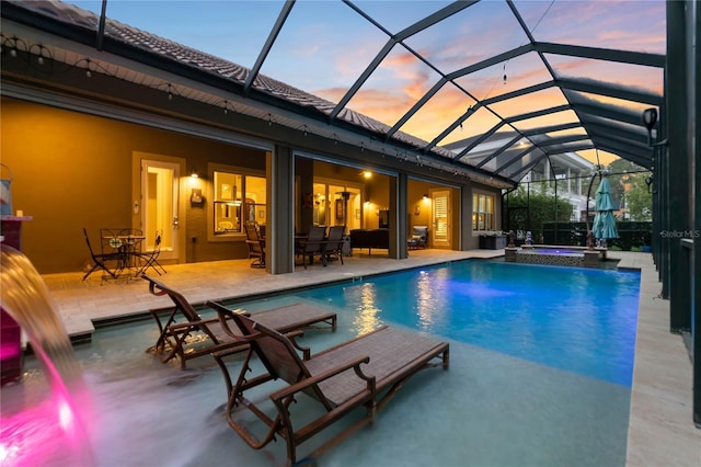 pool at dusk with an in ground hot tub, glass enclosure, and a patio