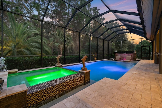 pool at dusk with a lanai, a patio area, and an in ground hot tub