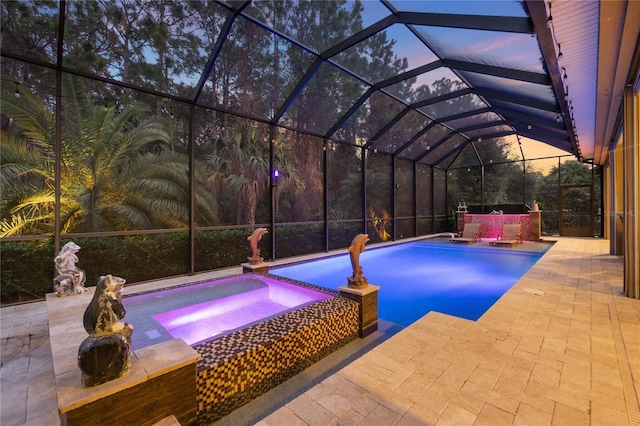 pool at dusk featuring an in ground hot tub, glass enclosure, and a patio