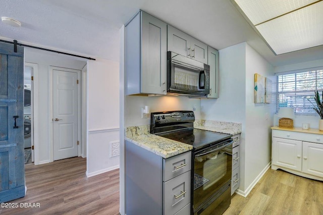 kitchen with gray cabinetry, a barn door, light hardwood / wood-style flooring, and black appliances