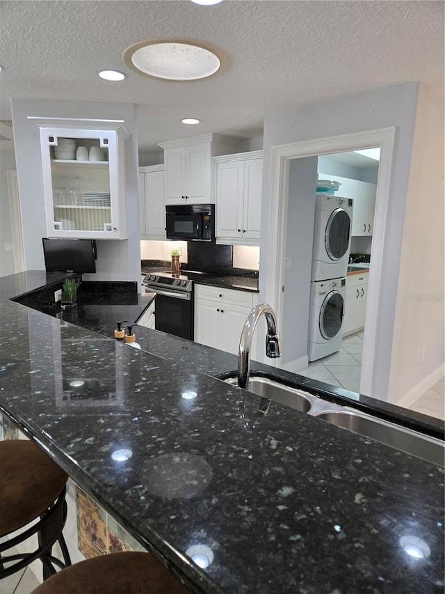 kitchen featuring stainless steel electric range oven, stacked washer / dryer, white cabinetry, dark stone counters, and a textured ceiling