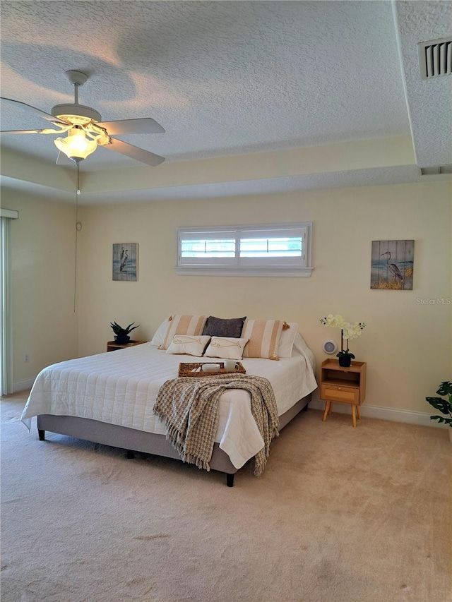 carpeted bedroom featuring ceiling fan, a tray ceiling, and a textured ceiling