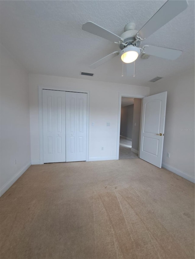 unfurnished bedroom with light carpet, ceiling fan, a closet, and a textured ceiling