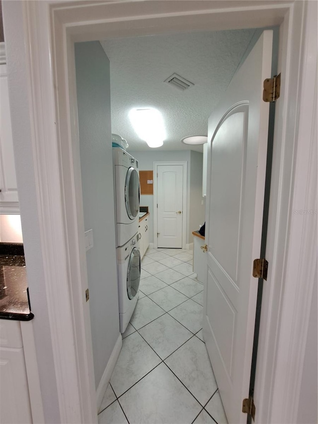 laundry room featuring light tile patterned floors, cabinets, a textured ceiling, and stacked washer / dryer