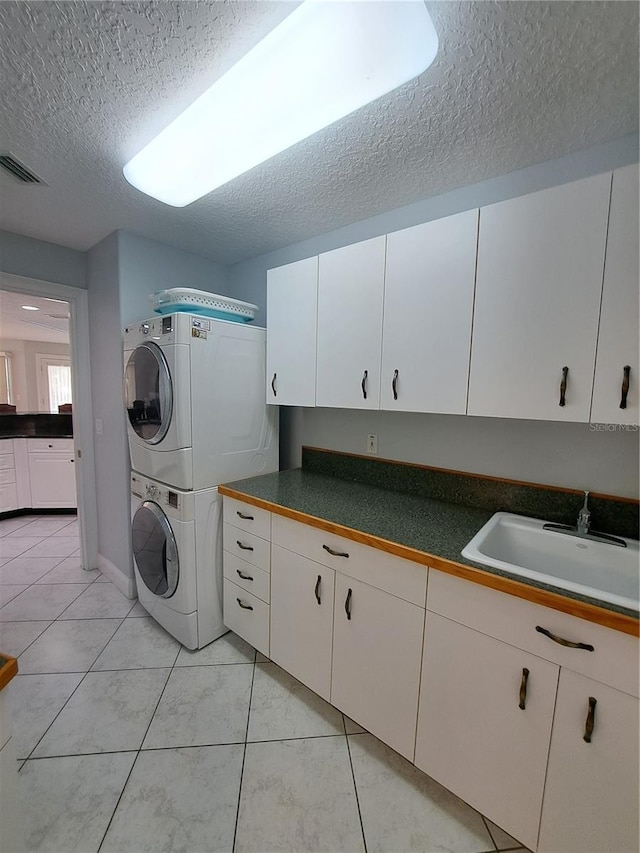 laundry room featuring stacked washer and dryer, cabinets, sink, and a textured ceiling