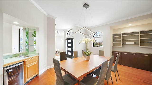 dining space featuring crown molding, sink, beverage cooler, and light hardwood / wood-style floors