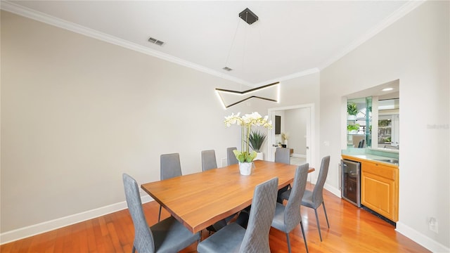 dining area featuring wine cooler, crown molding, and light hardwood / wood-style flooring