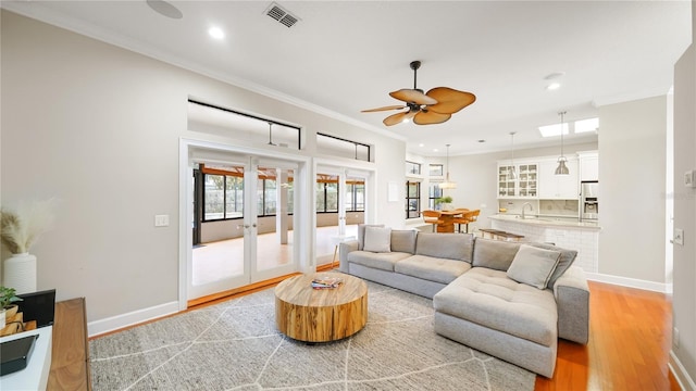 living room featuring crown molding, ceiling fan, light wood-type flooring, and french doors