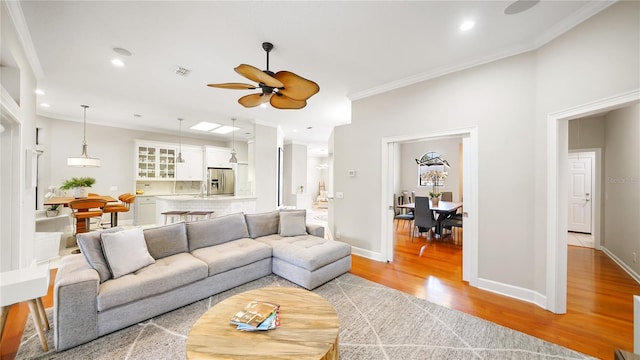 living room with ornamental molding, ceiling fan, and light wood-type flooring