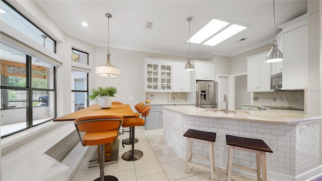 kitchen with decorative light fixtures, sink, a breakfast bar area, white cabinets, and stainless steel fridge