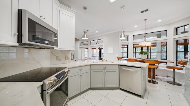 kitchen with appliances with stainless steel finishes, sink, hanging light fixtures, kitchen peninsula, and light stone countertops