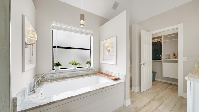 bathroom featuring tiled tub, vanity, hardwood / wood-style floors, and toilet