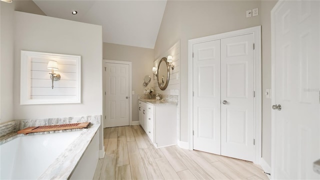 bathroom with vanity, vaulted ceiling, hardwood / wood-style floors, and a washtub