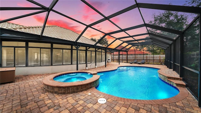 pool at dusk with an in ground hot tub, pool water feature, glass enclosure, and a patio area